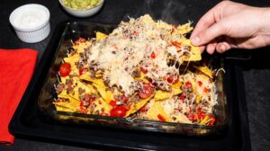Ovenschaal nacho's met SNX-gehakt, gesmolten kaas, paprika en cherrytomaatjes, met zure room en guacamole
